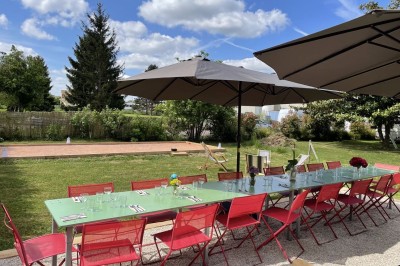 Terrasse aménagée avec tables, chaises et parasols devant une maison en pierre, entourée de verdure.