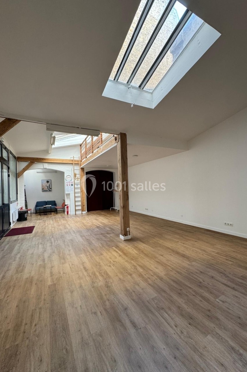 Intérieur d'une pièce lumineuse avec parquet, poutres en bois, verrière et mezzanine.