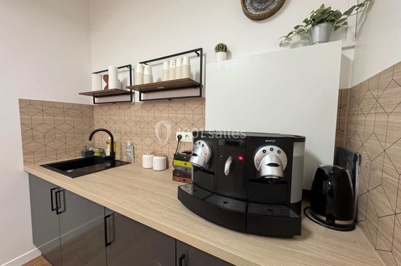 Cuisine moderne avec évier, machine à café automatique, bouilloire et étagères murales décorées.