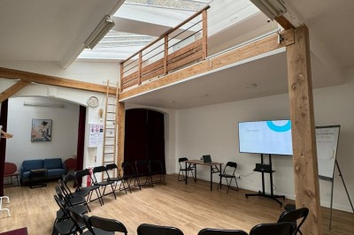Intérieur d'une pièce lumineuse avec parquet, poutres en bois, verrière et mezzanine.