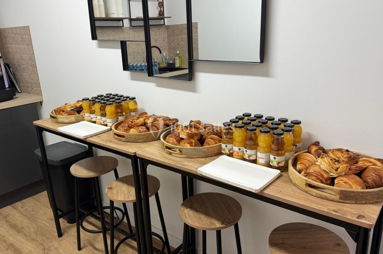 Plateau de viennoiseries et bouteilles de jus d'orange disposés sur une table haute dans une salle lumineuse.