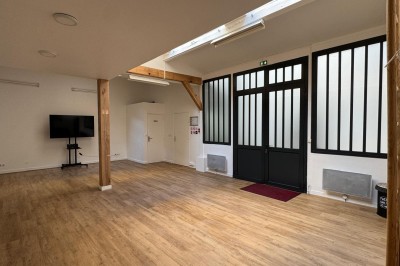 Intérieur d'une pièce lumineuse avec parquet, poutres en bois, verrière et mezzanine.