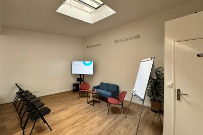 Salle lumineuse avec parquet, grande table entourée de chaises, écran, paperboard et mezzanine en bois.