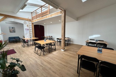 Salle lumineuse avec parquet, grande table entourée de chaises, écran, paperboard et mezzanine en bois.