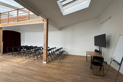 Salle lumineuse avec parquet, grande table entourée de chaises, écran, paperboard et mezzanine en bois.