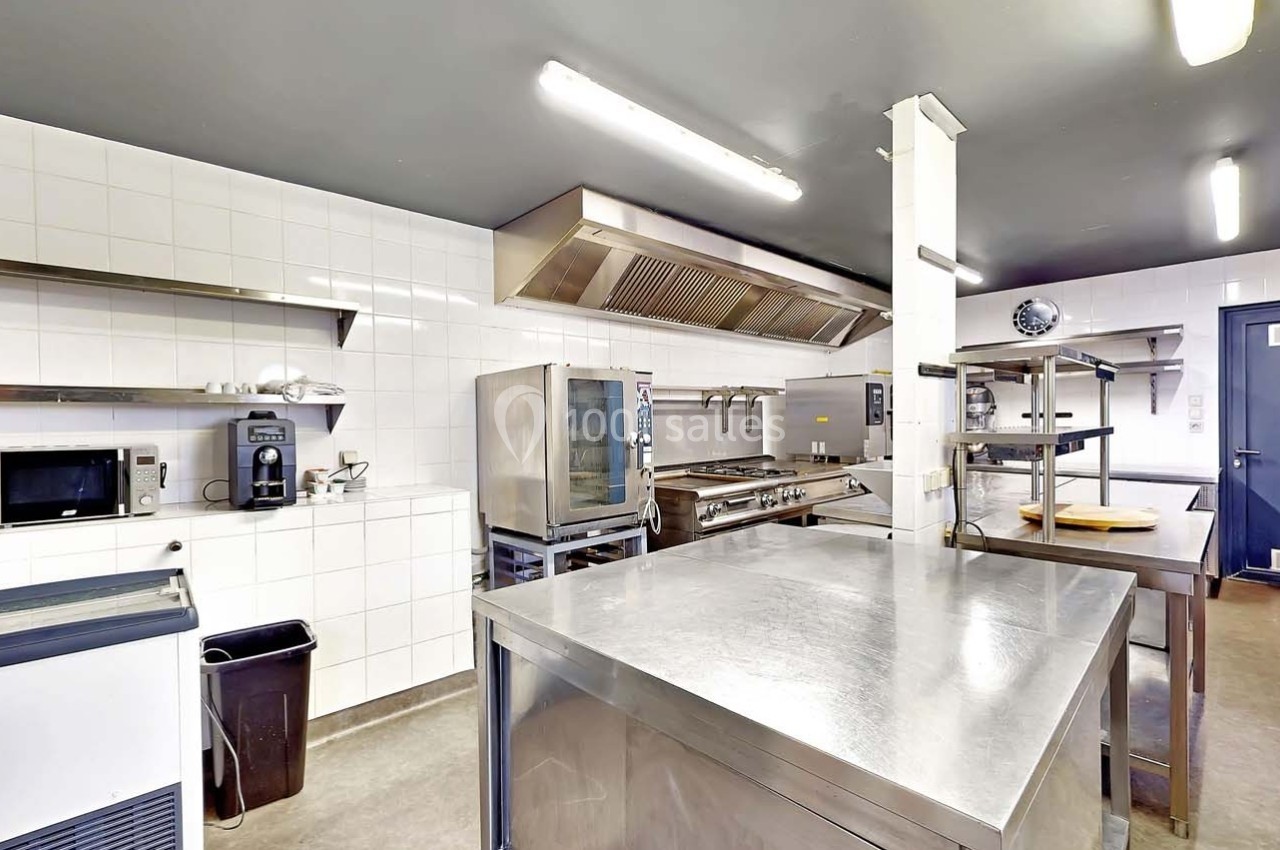 Cuisine professionnelle avec équipements en inox, plan de travail central, étagères murales et appareils électroménagers.