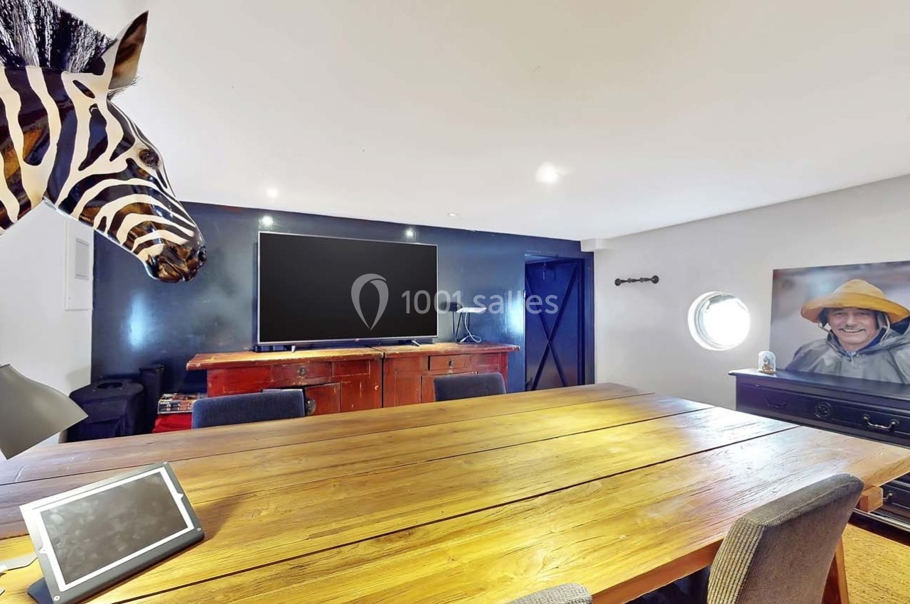 Salle de réunion avec une grande table en bois, un écran noir, une tête de zèbre décorative et une photo encadrée.