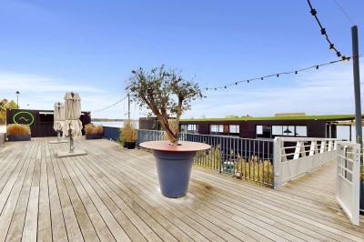 Miniature Location salle Tain-l'Hermitage (Drôme) - La Péniche #13 Terrasse en bois avec tables et chaises pliantes roses sous de grands parasols, entourée de plantes vertes.