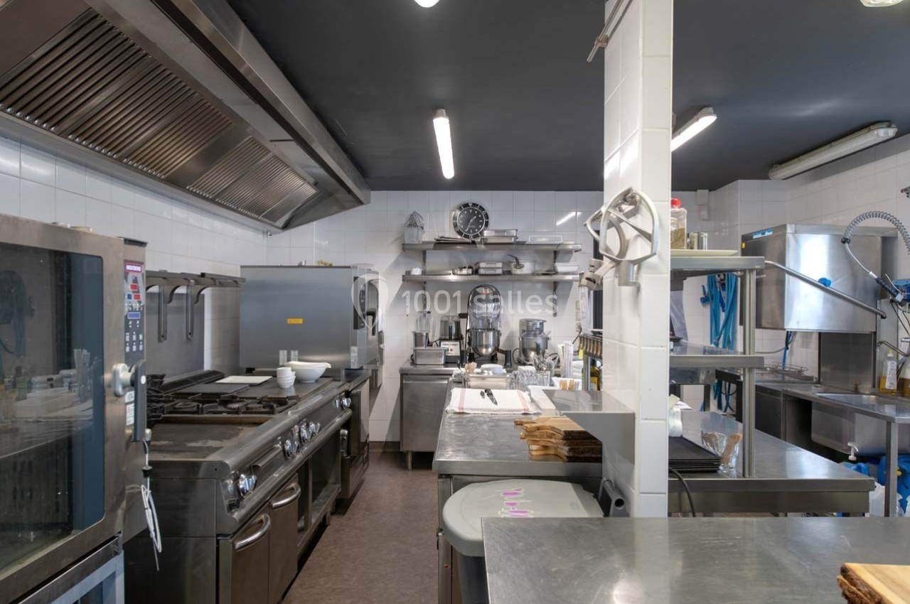 Cuisine professionnelle équipée avec des plans de travail en inox, appareils de cuisson et étagères de rangement.