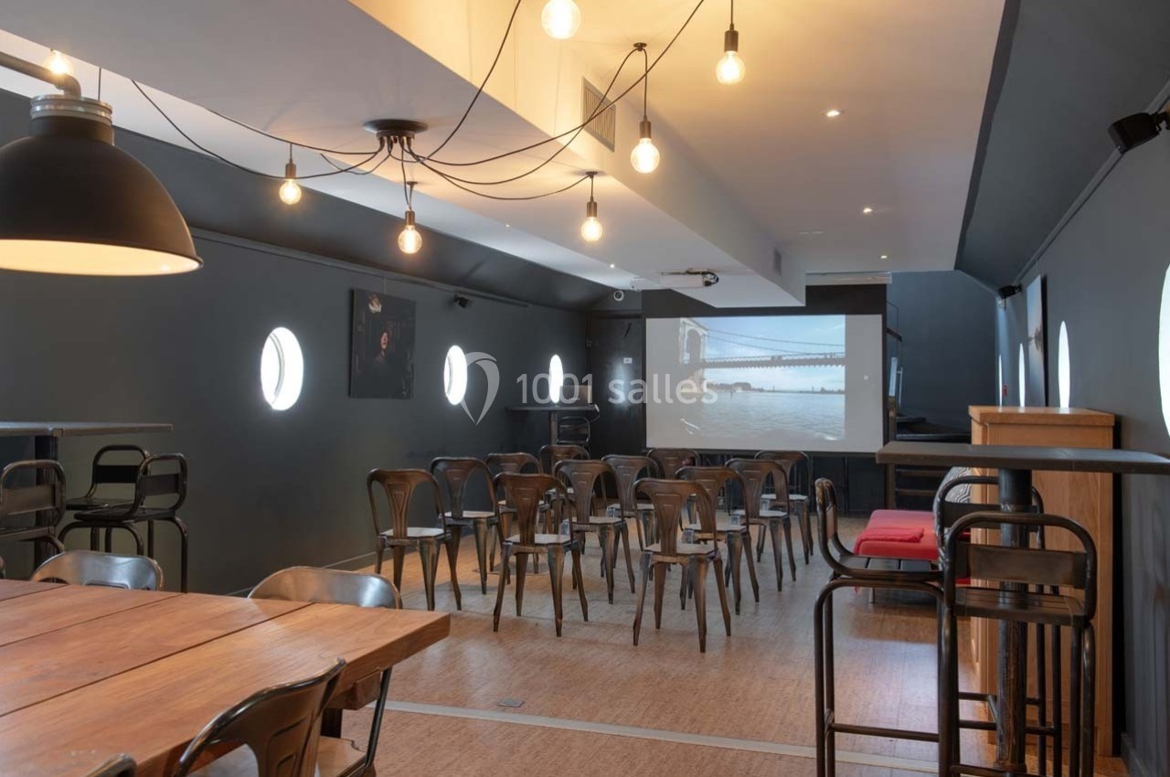 Salle aménagée avec des chaises disposées face à un écran de projection, éclairée par des suspensions lumineuses.