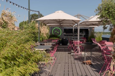 Miniature Location salle Tain-l'Hermitage (Drôme) - La Péniche #35 Terrasse en bois avec tables et chaises pliantes roses sous de grands parasols, entourée de plantes vertes.