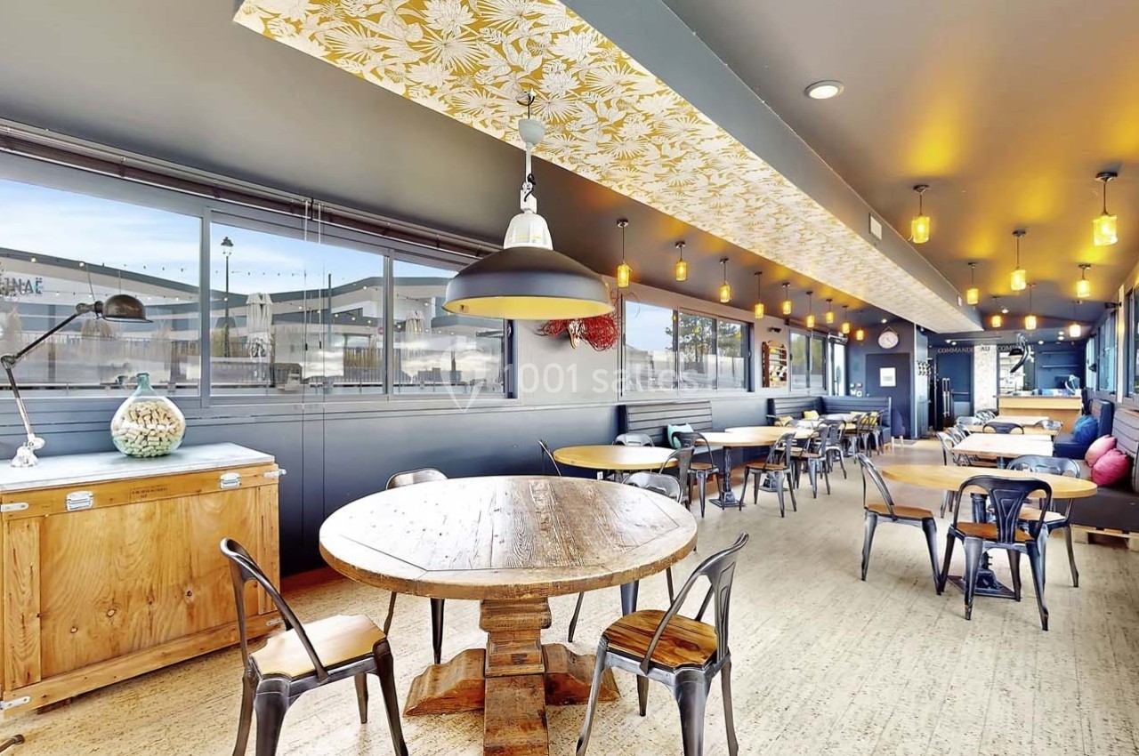 Salle de restaurant lumineuse avec tables en bois, chaises métalliques et plafond décoré de motifs floraux.