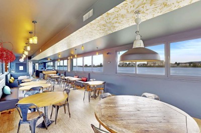 Miniature Location salle Tain-l'Hermitage (Drôme) - La Péniche #3 Terrasse ensoleillée avec tables et chaises pliantes roses sous de grands parasols, entourée de plantes vertes.