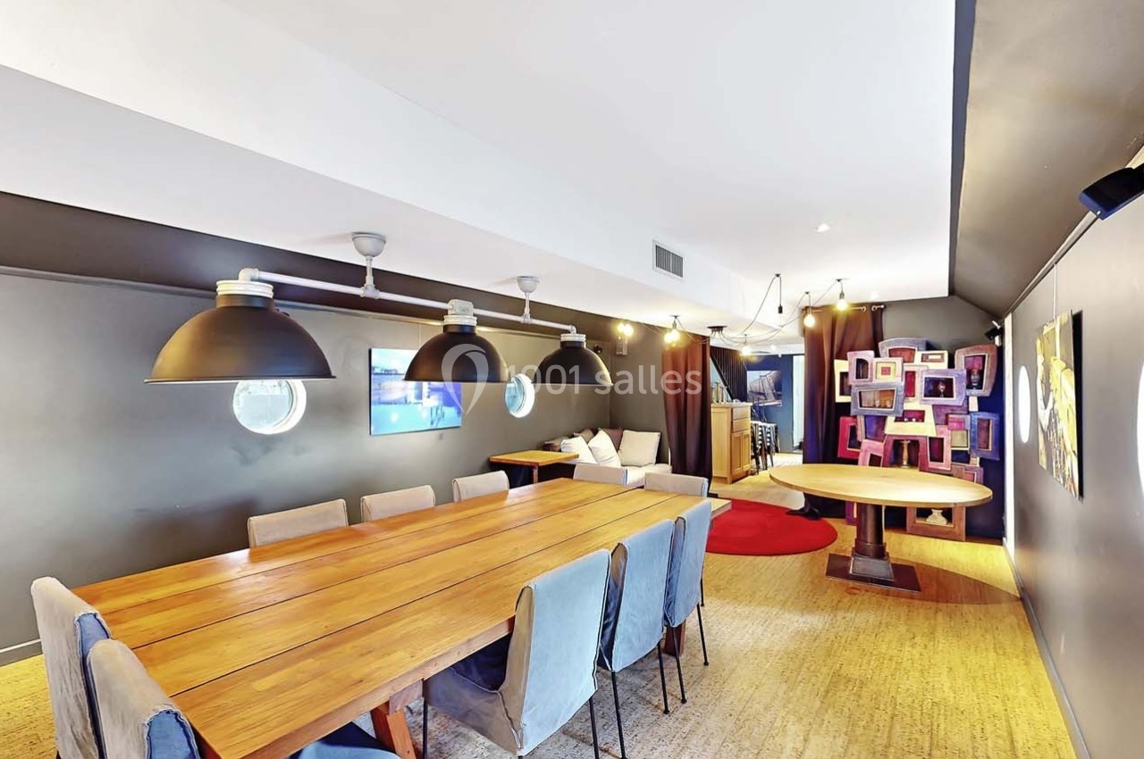 Salle moderne avec grande table en bois, chaises grises, luminaires suspendus et décoration murale colorée.