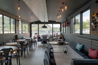 Miniature Location salle Tain-l'Hermitage (Drôme) - La Péniche #17 Terrasse ensoleillée avec tables et chaises pliantes roses sous de grands parasols, entourée de plantes vertes.