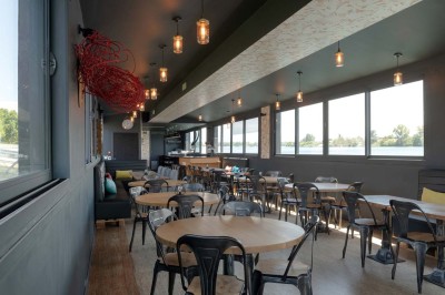 Miniature Location salle Tain-l'Hermitage (Drôme) - La Péniche #18 Terrasse ensoleillée avec tables et chaises pliantes roses sous de grands parasols, entourée de plantes vertes.