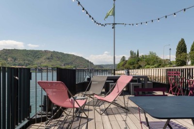 Miniature Location salle Tain-l'Hermitage (Drôme) - La Péniche #23 Terrasse ensoleillée avec tables et chaises pliantes roses sous de grands parasols, entourée de plantes vertes.