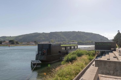 Miniature Location salle Tain-l'Hermitage (Drôme) - La Péniche #30 Terrasse ensoleillée avec tables et chaises pliantes roses sous de grands parasols, entourée de plantes vertes.