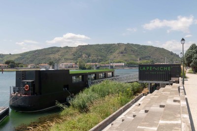 Miniature Location salle Tain-l'Hermitage (Drôme) - La Péniche #39 Terrasse ensoleillée avec tables et chaises pliantes roses sous de grands parasols, entourée de plantes vertes.