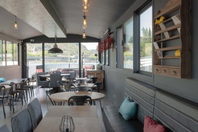 Miniature Location salle Tain-l'Hermitage (Drôme) - La Péniche #41 Terrasse ensoleillée avec tables et chaises pliantes roses sous de grands parasols, entourée de plantes vertes.