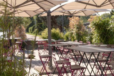 Miniature Location salle Tain-l'Hermitage (Drôme) - La Péniche #43 Terrasse ensoleillée avec tables et chaises pliantes roses sous de grands parasols, entourée de plantes vertes.