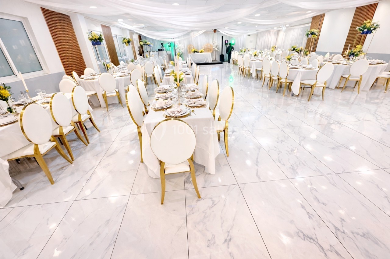 Salle de réception élégante avec tables dressées, chaises blanches et décorations florales sous un plafond drapé.