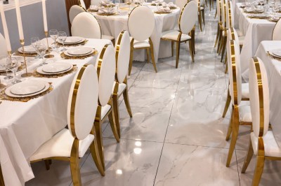 Salle de réception avec tables dressées, nappes blanches, chaises dorées et arrangements floraux jaunes et blancs.