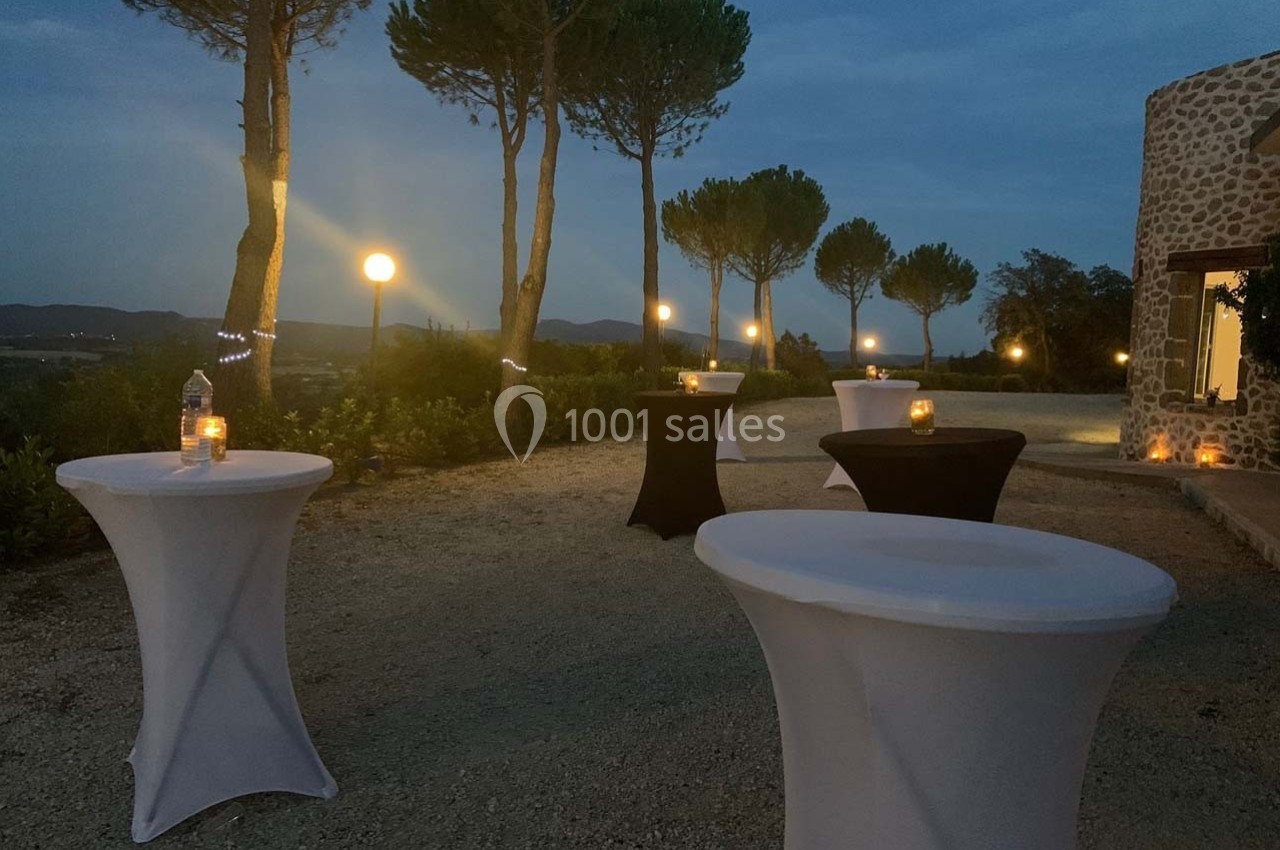 Tables hautes dressées en extérieur au crépuscule, entourées de bougies et éclairées par des lampadaires.