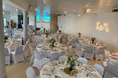 Chaises blanches alignées en extérieur face à une arche décorée, avec vue sur un paysage vallonné et des arbres.