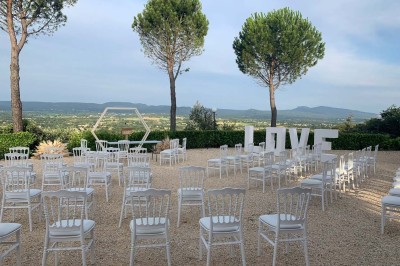 Chaises blanches alignées en extérieur face à une arche décorée, avec vue sur un paysage vallonné et des arbres.