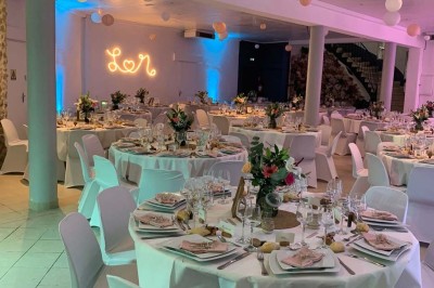 Chaises blanches alignées en extérieur face à une arche décorée, avec vue sur un paysage vallonné et des arbres.