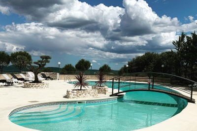 Chaises blanches alignées en extérieur face à une arche décorée, avec vue sur un paysage vallonné et des arbres.