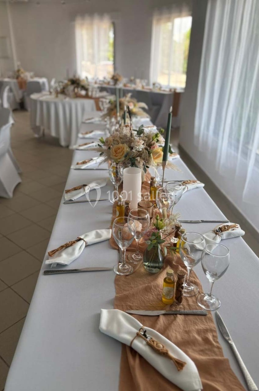 Table décorée pour un événement, avec nappes blanches, bougies, fleurs, serviettes pliées et verres disposés.