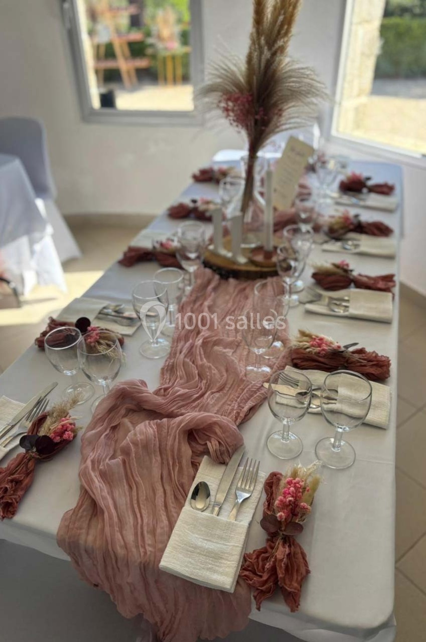 Table élégamment dressée avec une nappe blanche, chemin de table rose, couverts, verres et décorations florales.