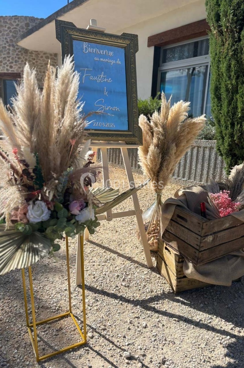 Panneau de bienvenue pour un mariage entouré de décorations florales avec des pampas et des caisses en bois.
