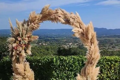 Chaises blanches alignées en extérieur face à une arche décorée, avec vue sur un paysage vallonné et des arbres.