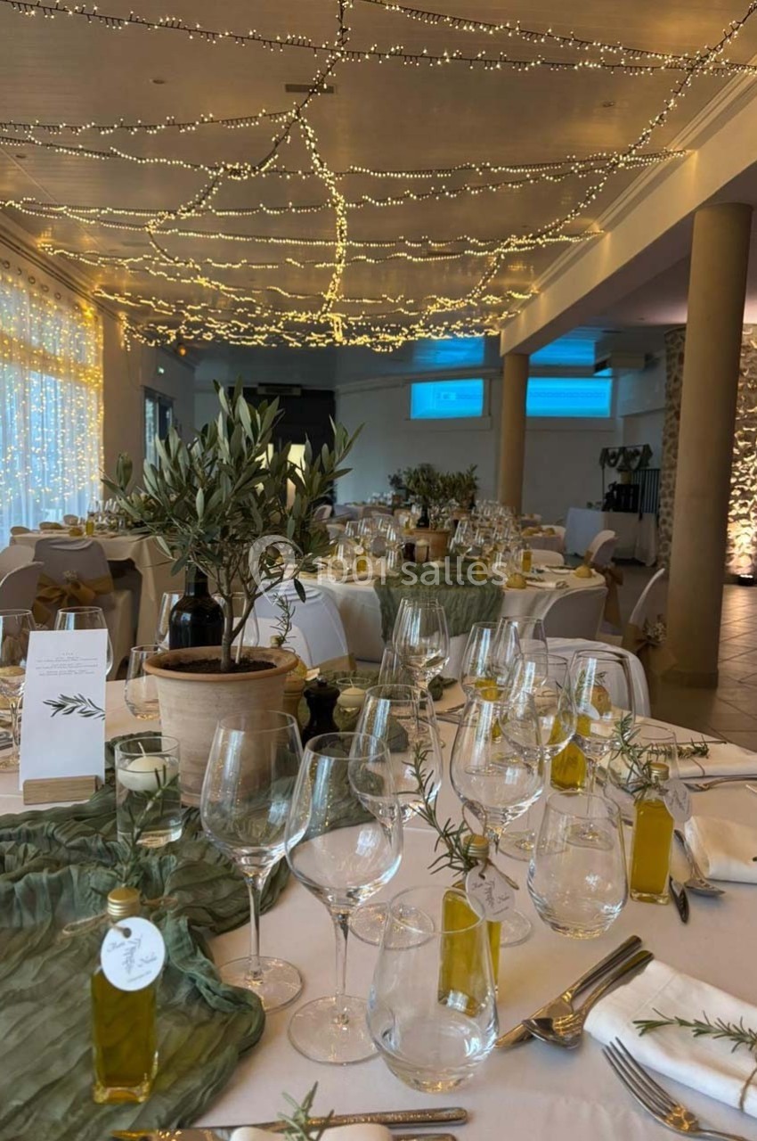 Salle de réception décorée avec des guirlandes lumineuses, tables dressées avec vaisselle élégante et bouteilles d'huile d…