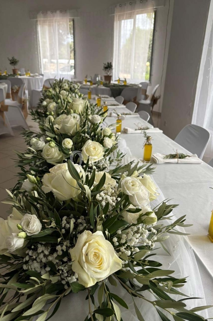 Décoration de table avec des roses blanches, gypsophiles et feuillage, dans une salle lumineuse avec nappes blanches.