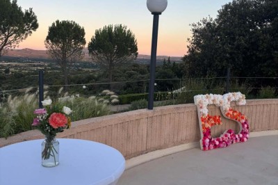 Chaises blanches alignées en extérieur face à une arche décorée, avec vue sur un paysage vallonné et des arbres.