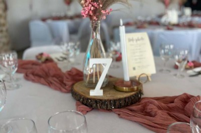 Chaises blanches alignées en extérieur face à une arche décorée, avec vue sur un paysage vallonné et des arbres.