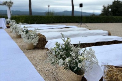 Chaises blanches alignées en extérieur face à une arche décorée, avec vue sur un paysage vallonné et des arbres.