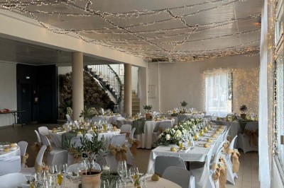 Chaises blanches alignées en extérieur face à une arche décorée, avec vue sur un paysage vallonné et des arbres.