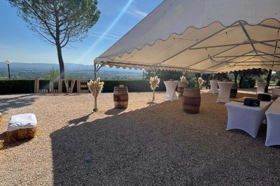 Chaises blanches alignées en extérieur face à une arche décorée, avec vue sur un paysage vallonné et des arbres.