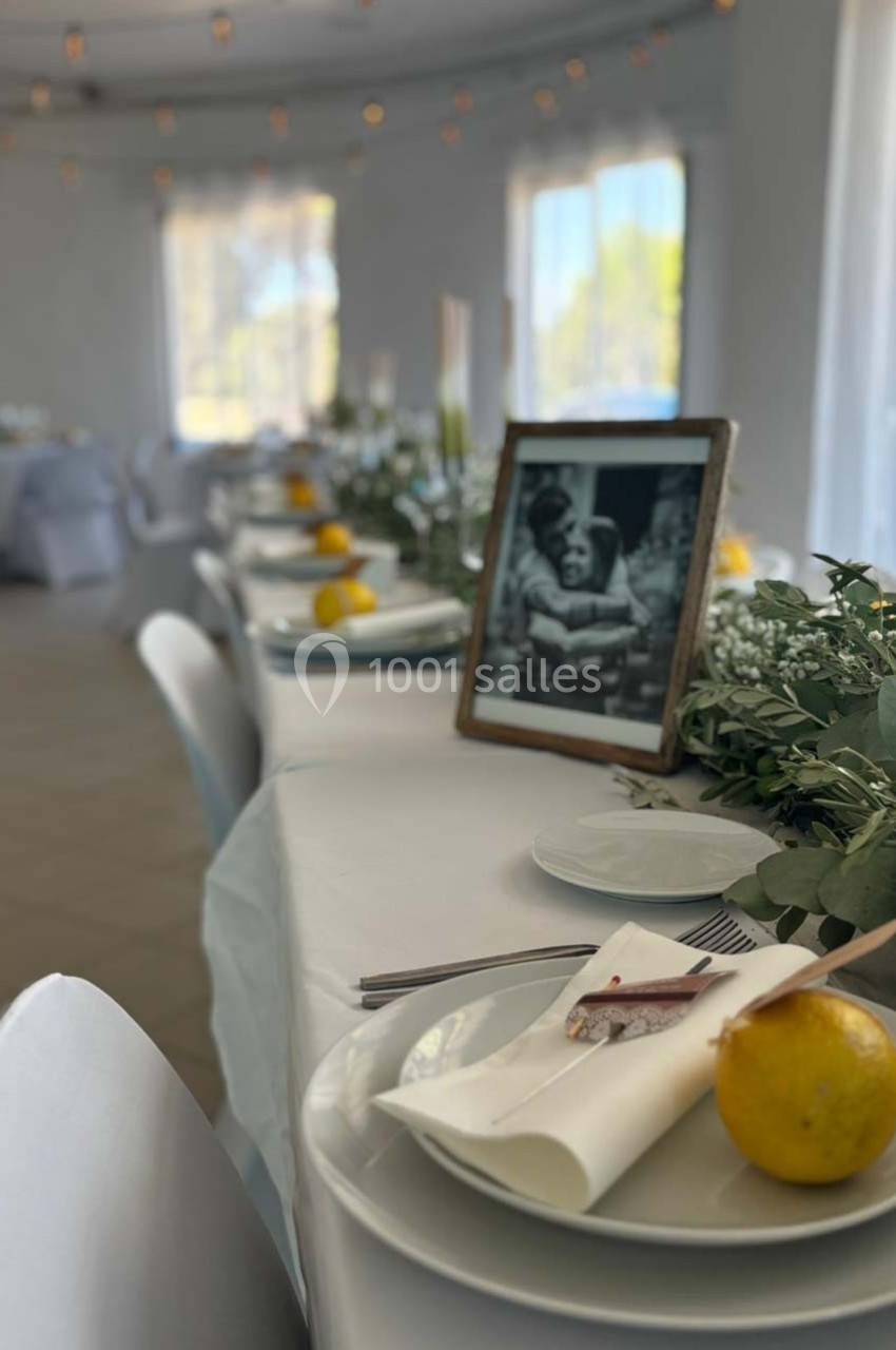 Table décorée avec nappe blanche, citrons, verdure, photo encadrée et lumière naturelle entrant par les fenêtres.