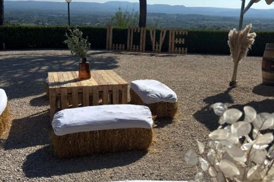 Chaises blanches alignées en extérieur face à une arche décorée, avec vue sur un paysage vallonné et des arbres.