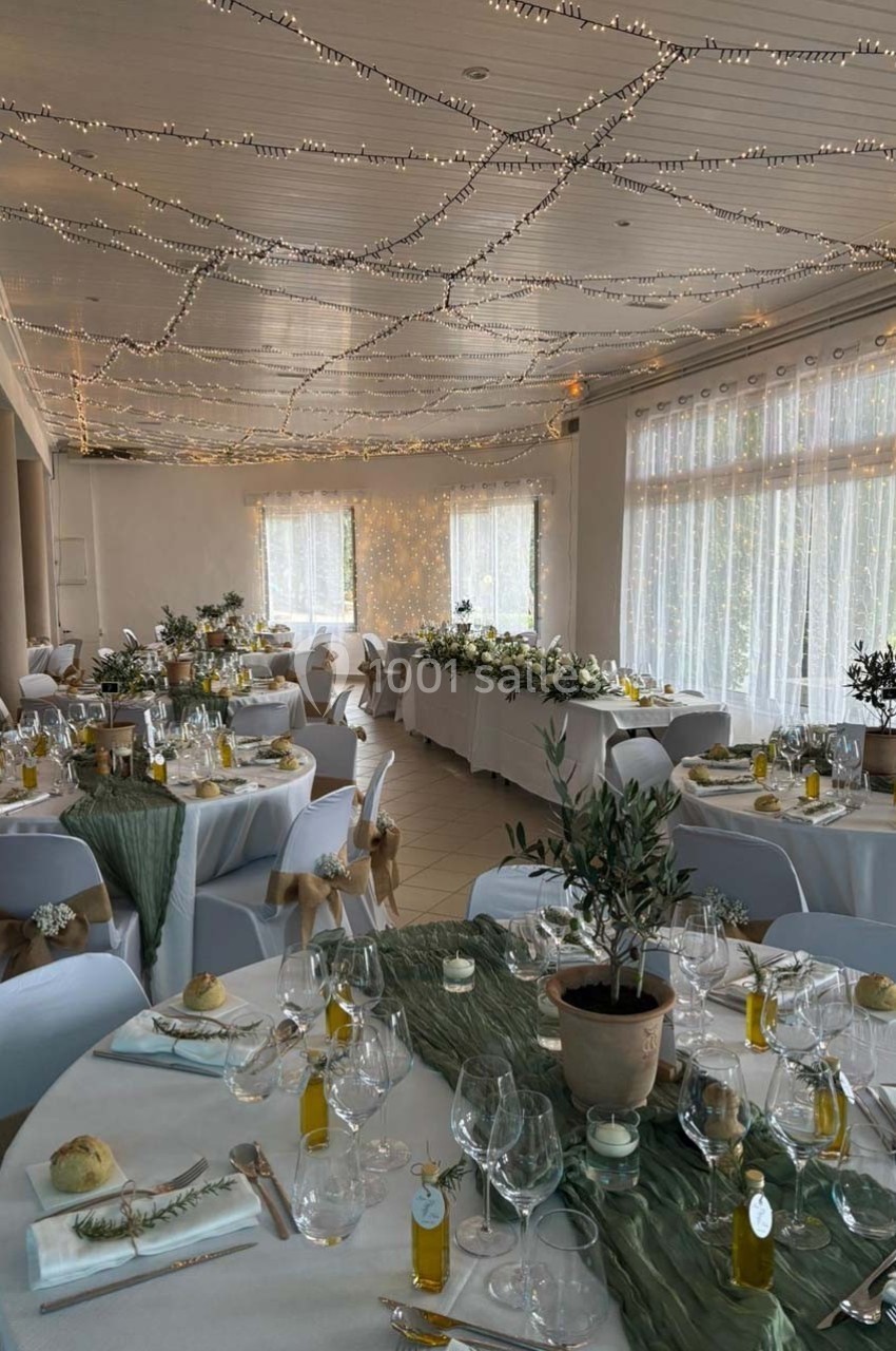 Salle de réception décorée avec des tables élégantes, nappes blanches, centres de table végétaux et guirlandes lumineuses au…