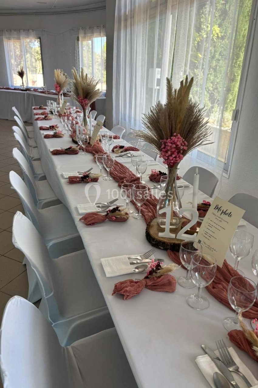 Table de réception décorée avec nappes blanches, chemins de table roses, bouquets de fleurs séchées et vaisselle élégante.