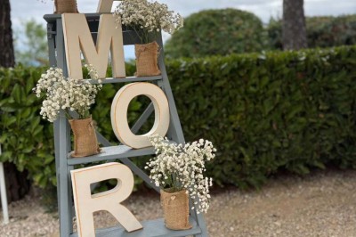 Chaises blanches alignées en extérieur face à une arche décorée, avec vue sur un paysage vallonné et des arbres.