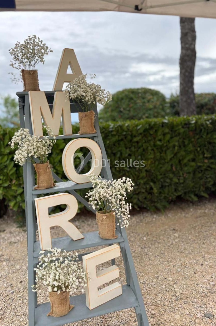 Échelle décorative avec des lettres formant ’AMORE’ et des bouquets de gypsophiles dans des pots en toile de jute.