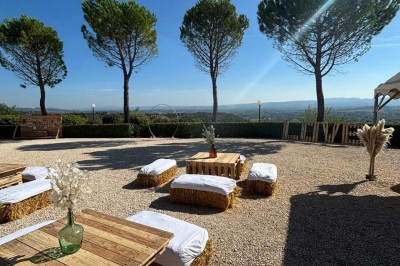 Chaises blanches alignées en extérieur face à une arche décorée, avec vue sur un paysage vallonné et des arbres.